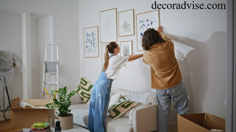 Two people hanging framed wall art in a white living room during home decoration.